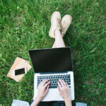 View from above of student sitting in grass using their laptop computer