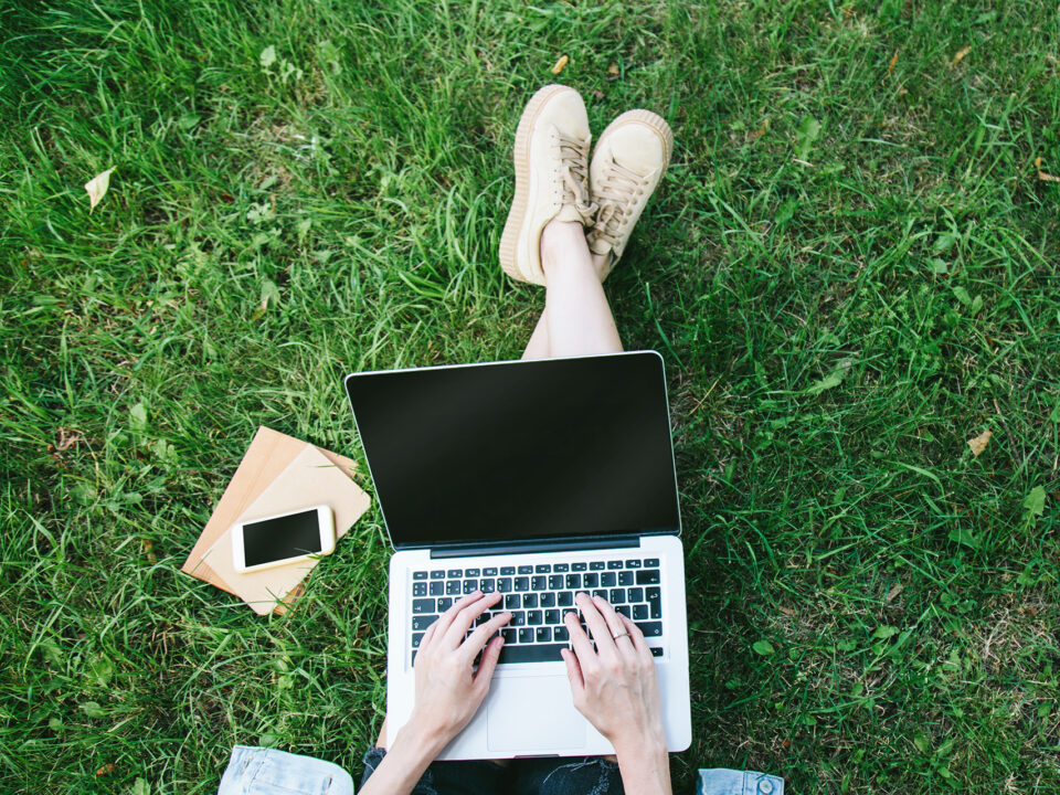 View from above of student sitting in grass using their laptop computer